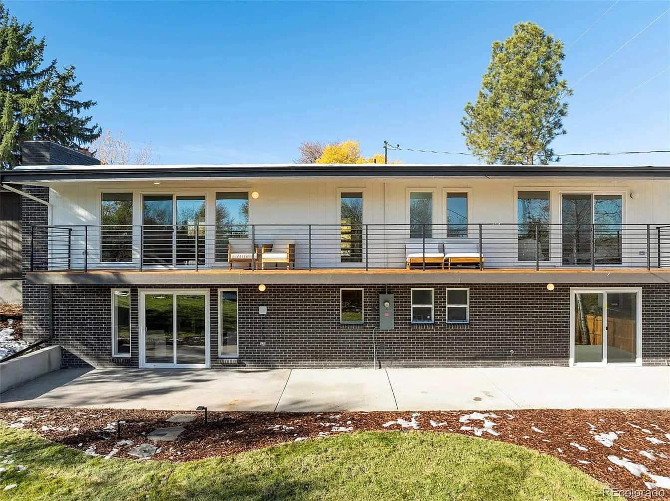 Two-story house with white siding, black accents, and balconies, set against a blue sky and green lawn.
