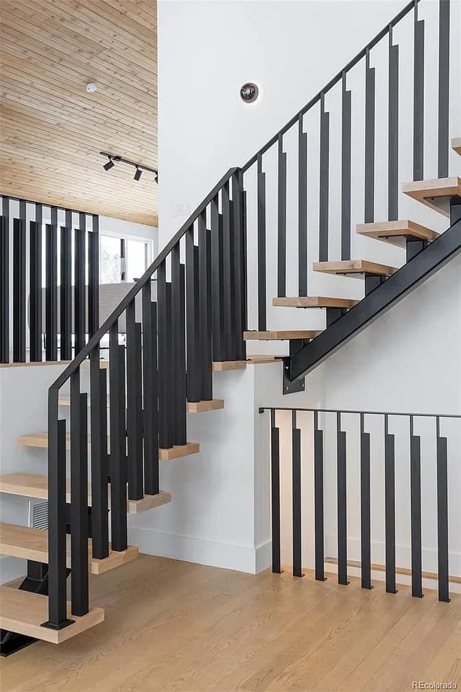 Modern interior staircase with black metal railings and wooden steps.