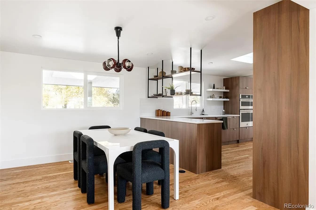 Modern dining room with wooden floors, white walls, and a dark wood kitchen.