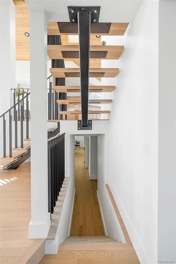 Modern staircase with wooden treads, black support beams, and white walls leading to a hallway.