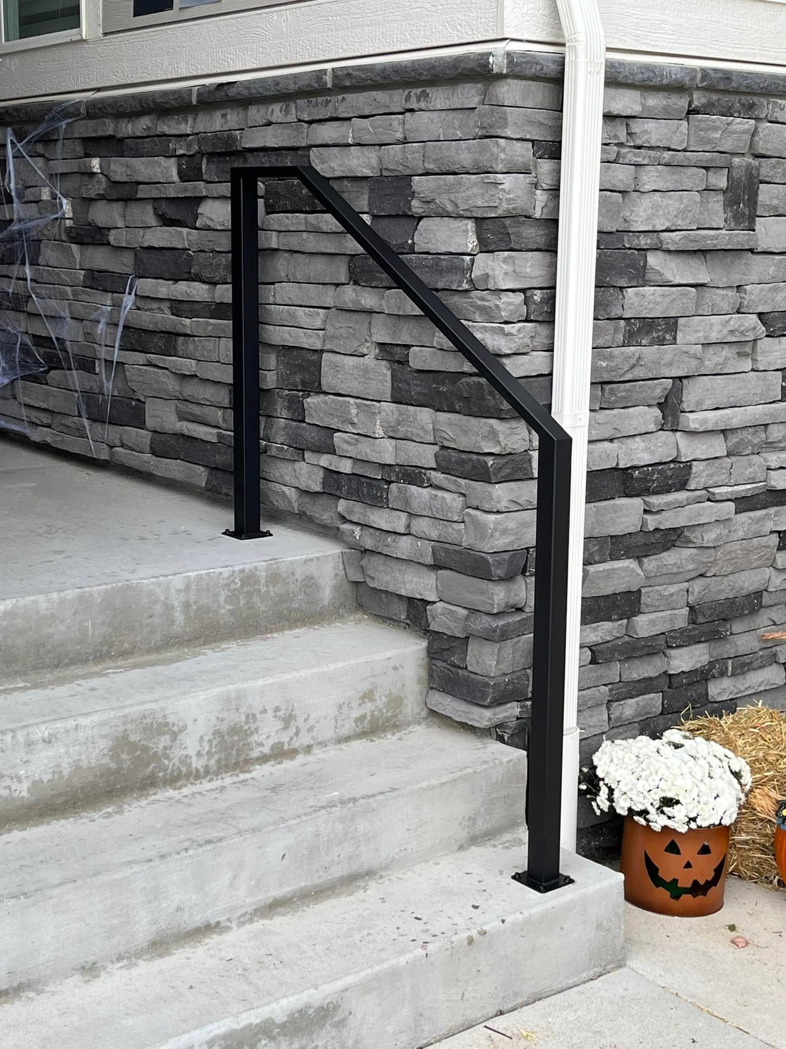 Black metal handrail on concrete steps, against a stone facade.