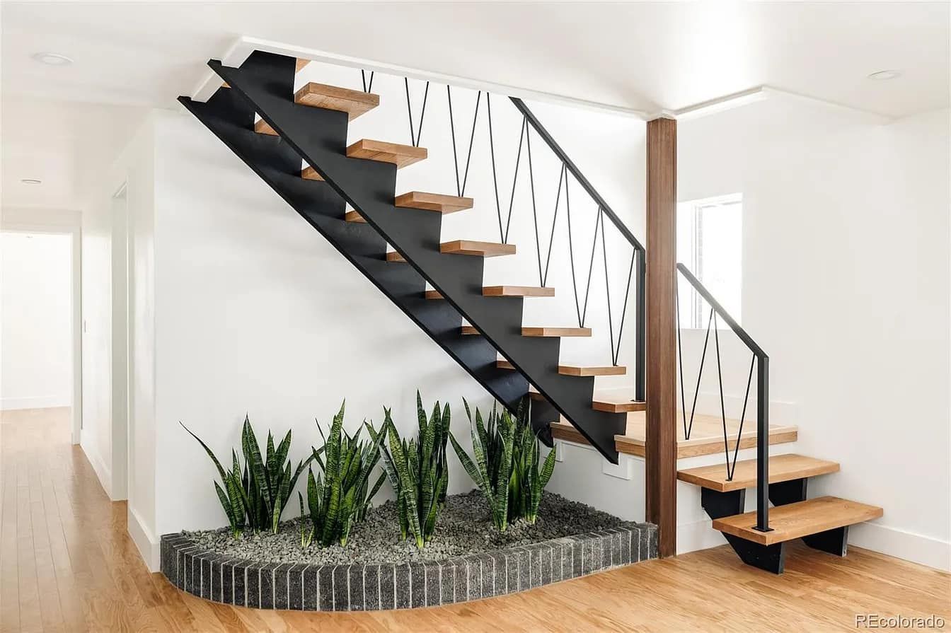 Modern staircase with wooden steps, black railing, and a planter with snake plants.