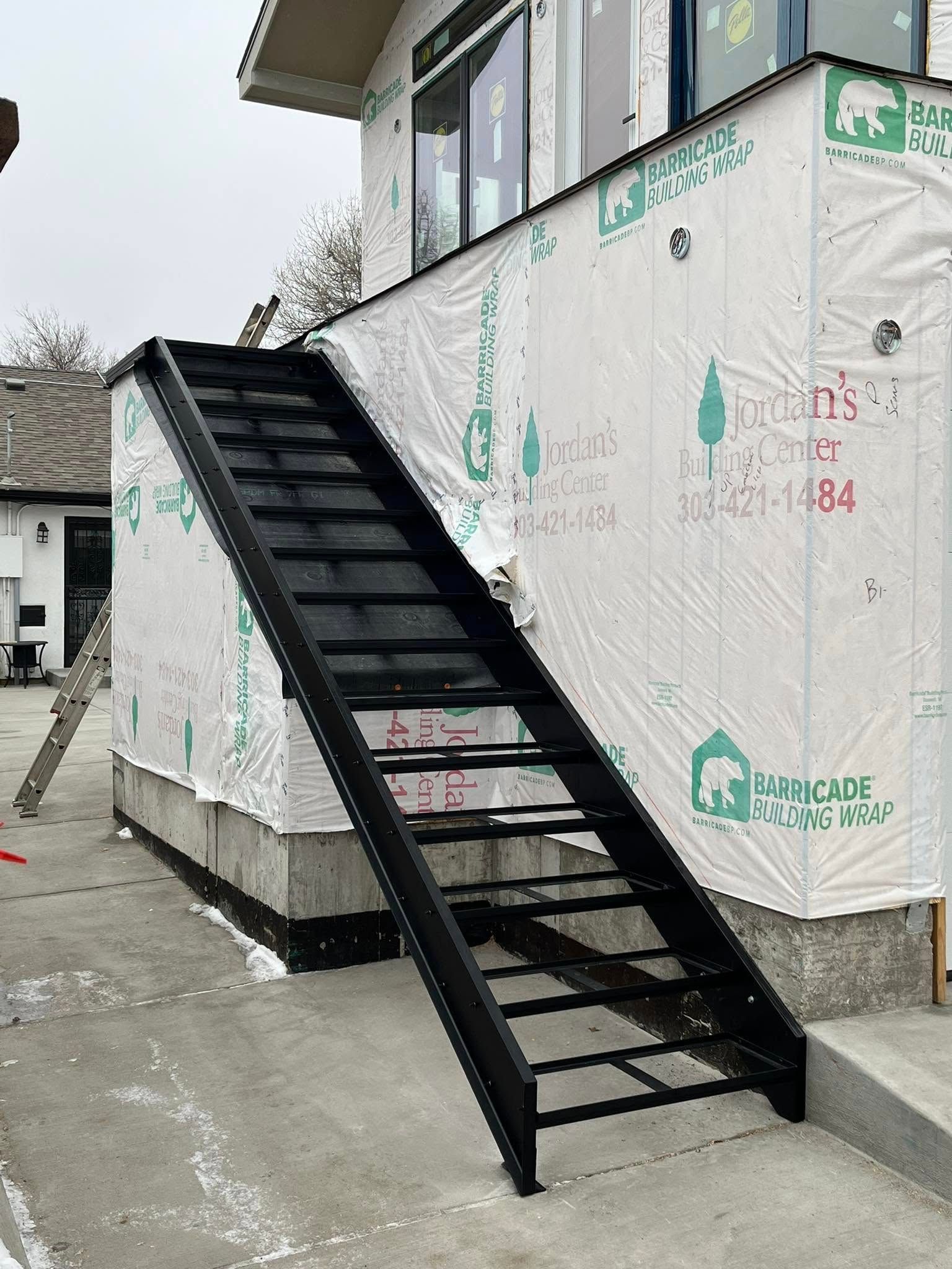 Black metal staircase leading up to a building's second story; exterior view on a cloudy day.