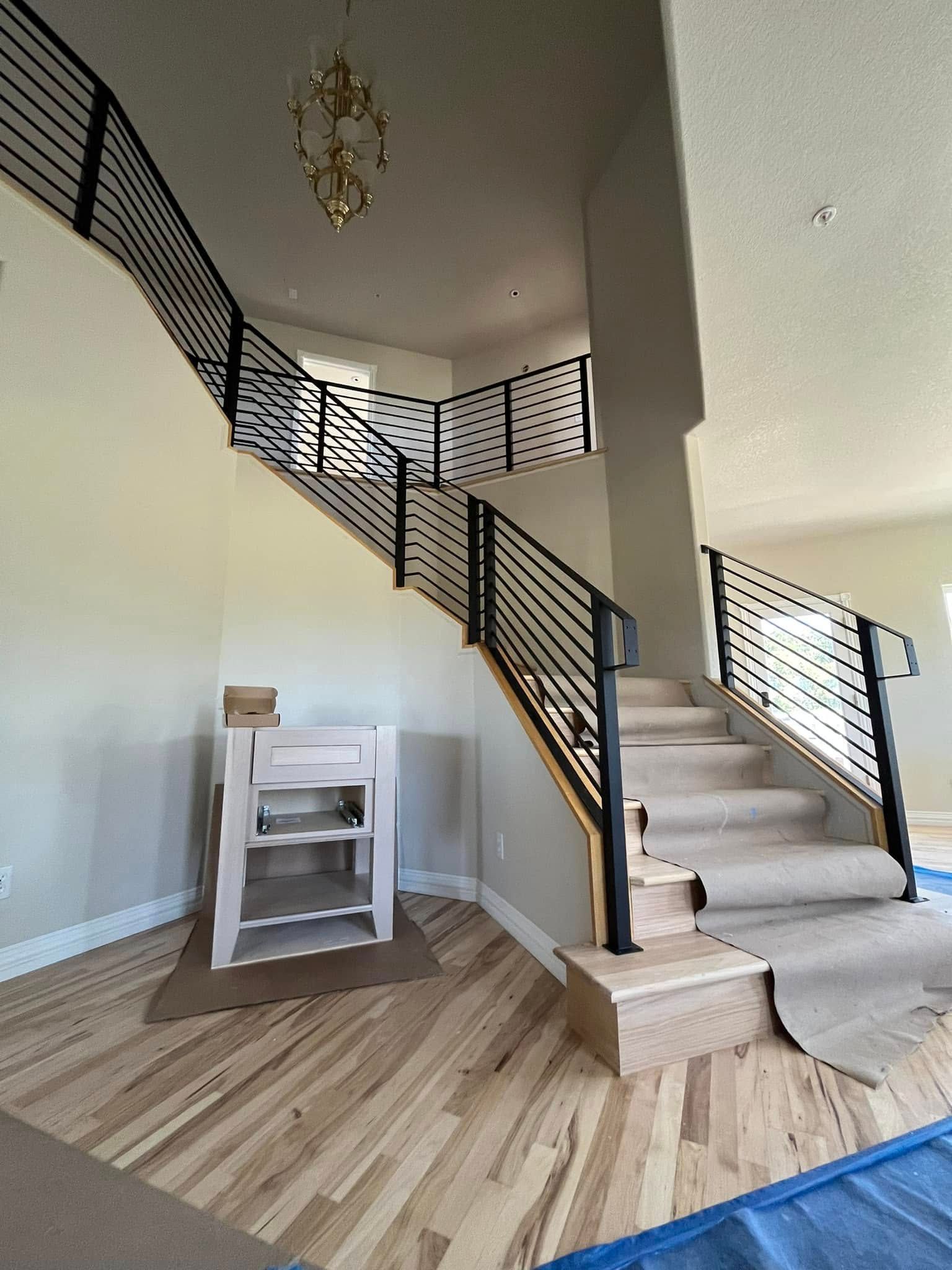 Two-story entry with wooden stairs and black metal railing. Light wood floor and cream walls.