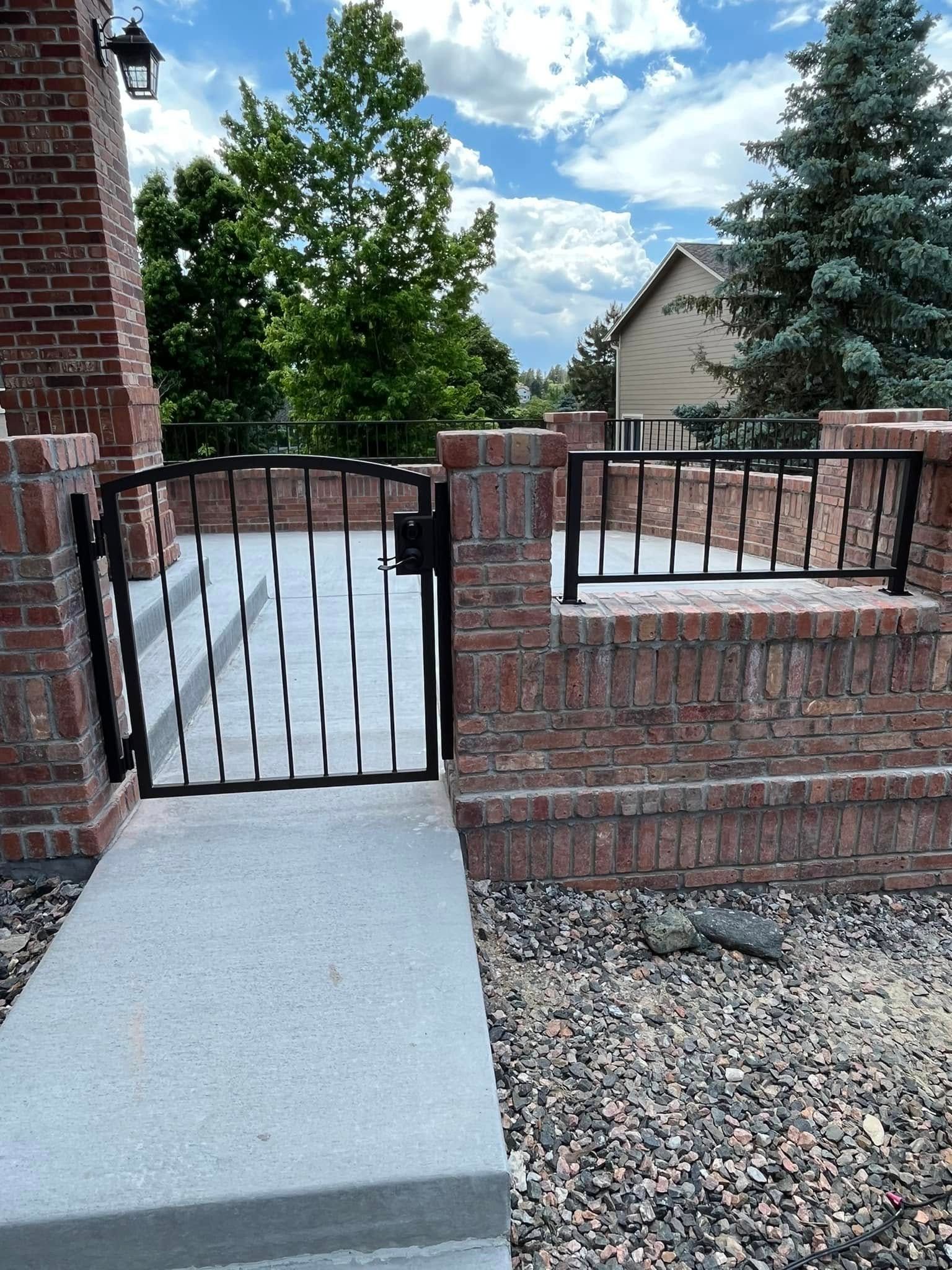 Black wrought iron gate and railing on a brick porch. Blue sky and greenery in the background.
