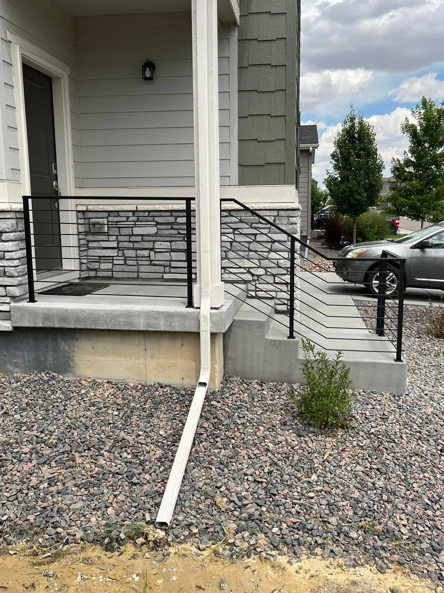 A home's front porch with black metal railings, stone accents, concrete steps, and a downspout.