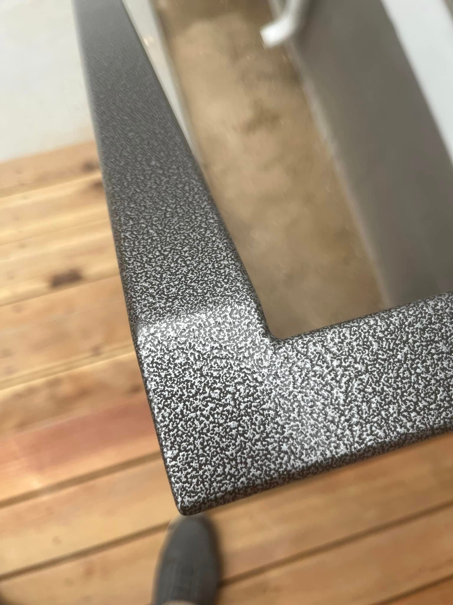 Corner of a textured, black metal frame on wooden planks, with a gray shoe visible.
