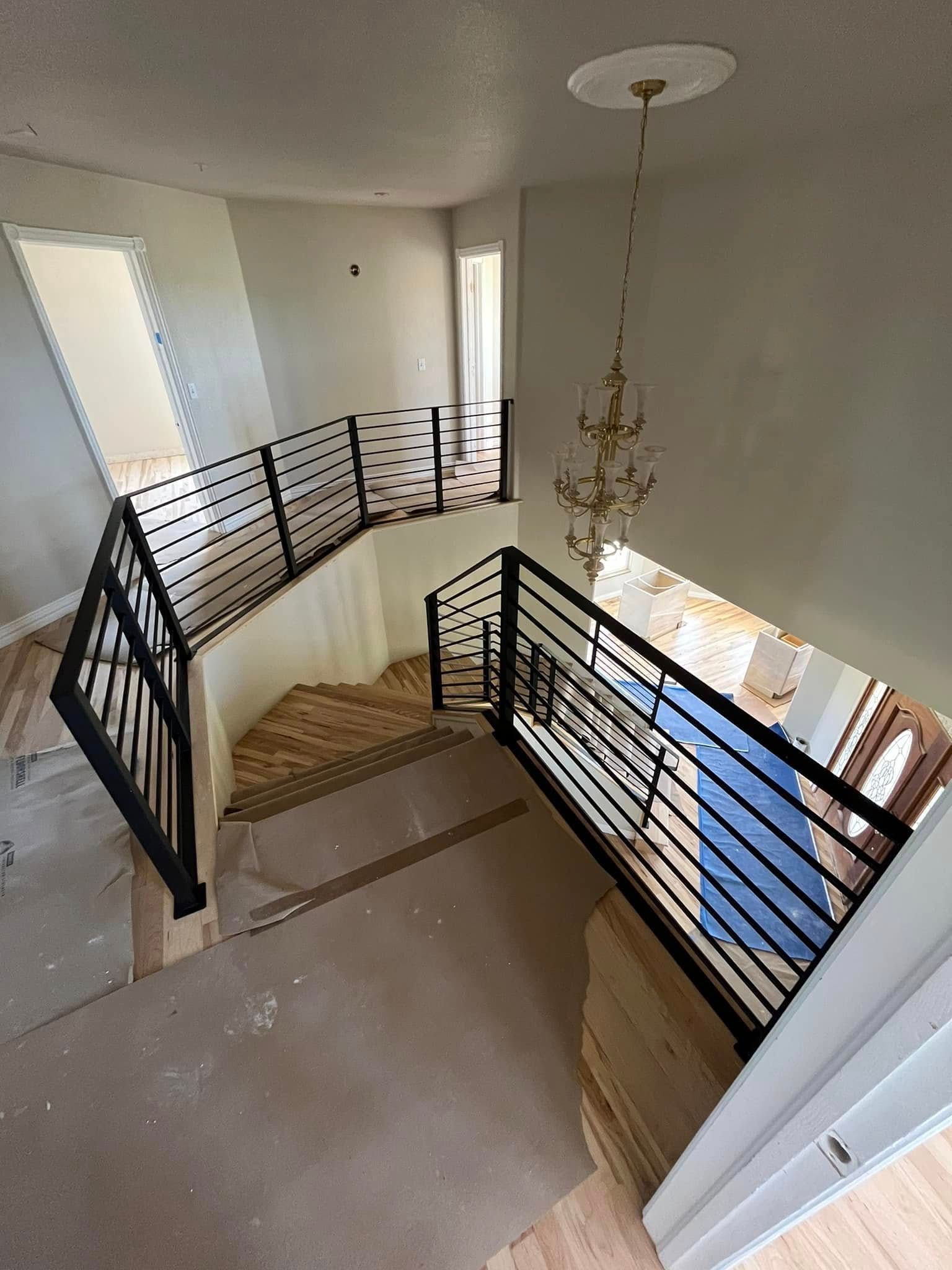 A modern black railing surrounds a staircase with wooden steps. View is from above.