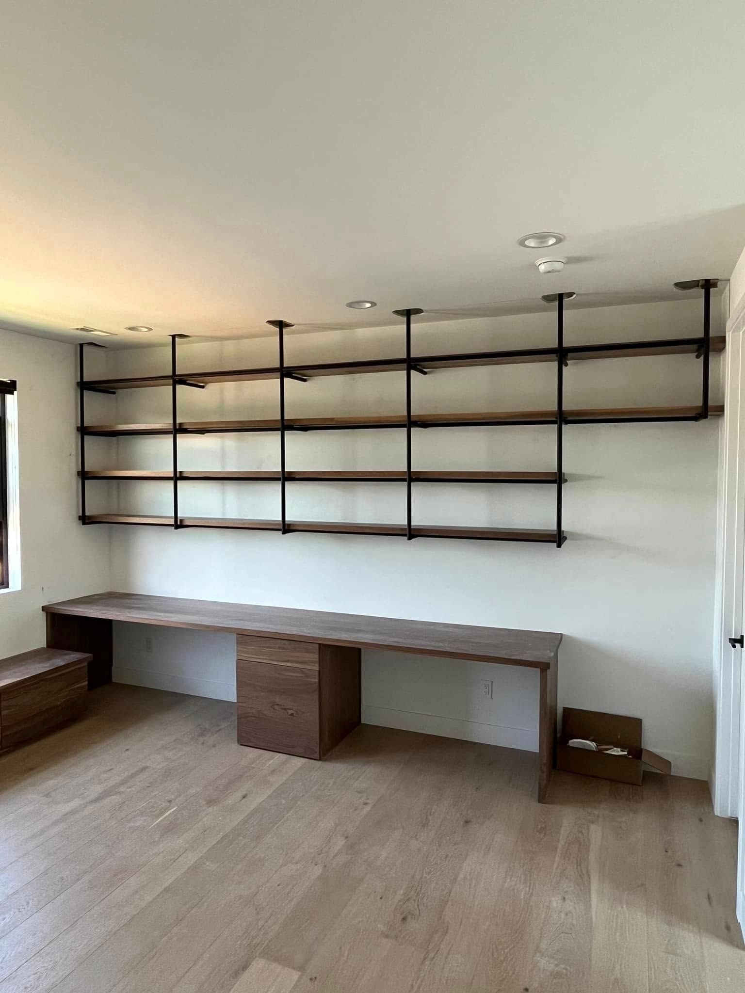Built-in office with dark wood shelving above a desk, supported by black pipes, against a white wall.