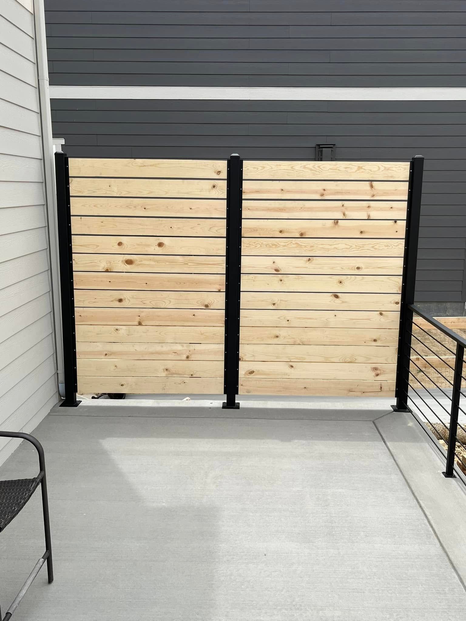 Wooden horizontal slat fence on a concrete patio with black posts.