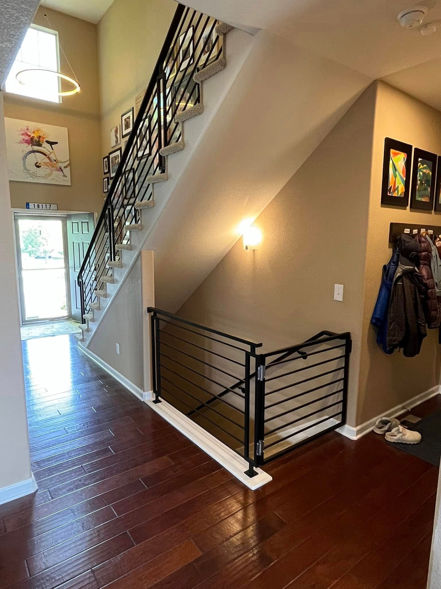 A staircase in a foyer. Hardwood floors, a white door, and artwork adorn the walls.