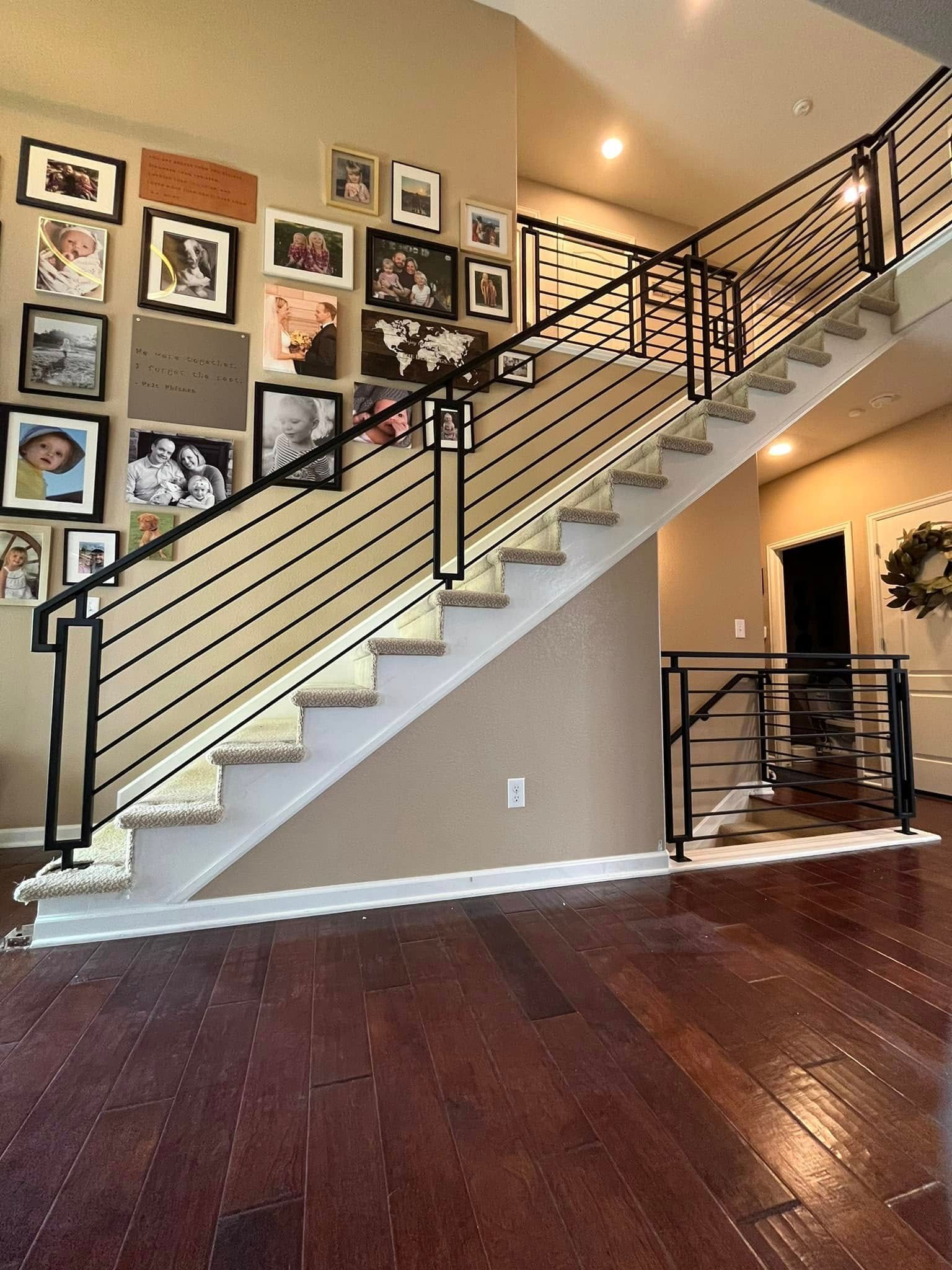 A staircase with black metal railings, dark wood floors, and a wall of framed photos.