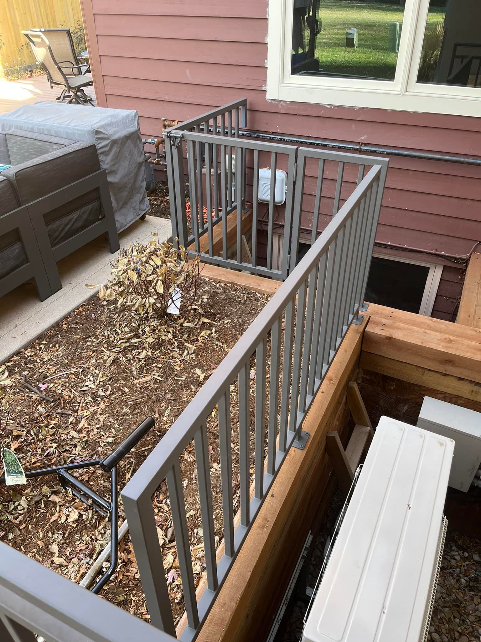 Gray metal railing surrounds a sunken outdoor area with a small electrical box.