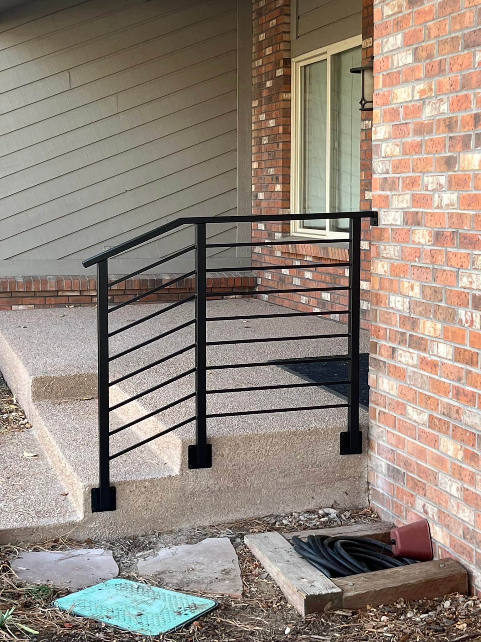 Black metal handrail on concrete steps next to brick wall and siding.