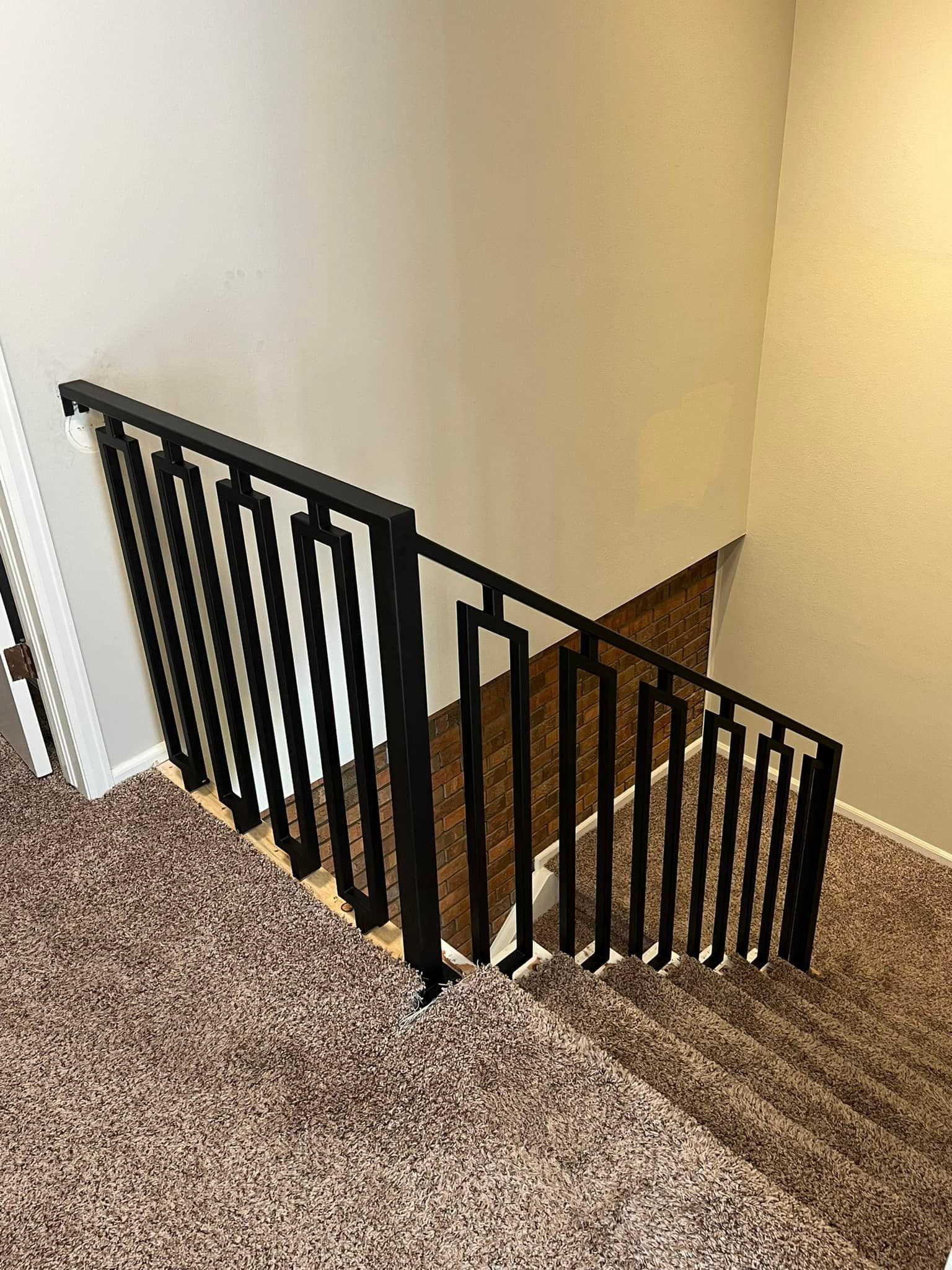 Black railing next to carpeted stairs leading down. Beige walls surround.
