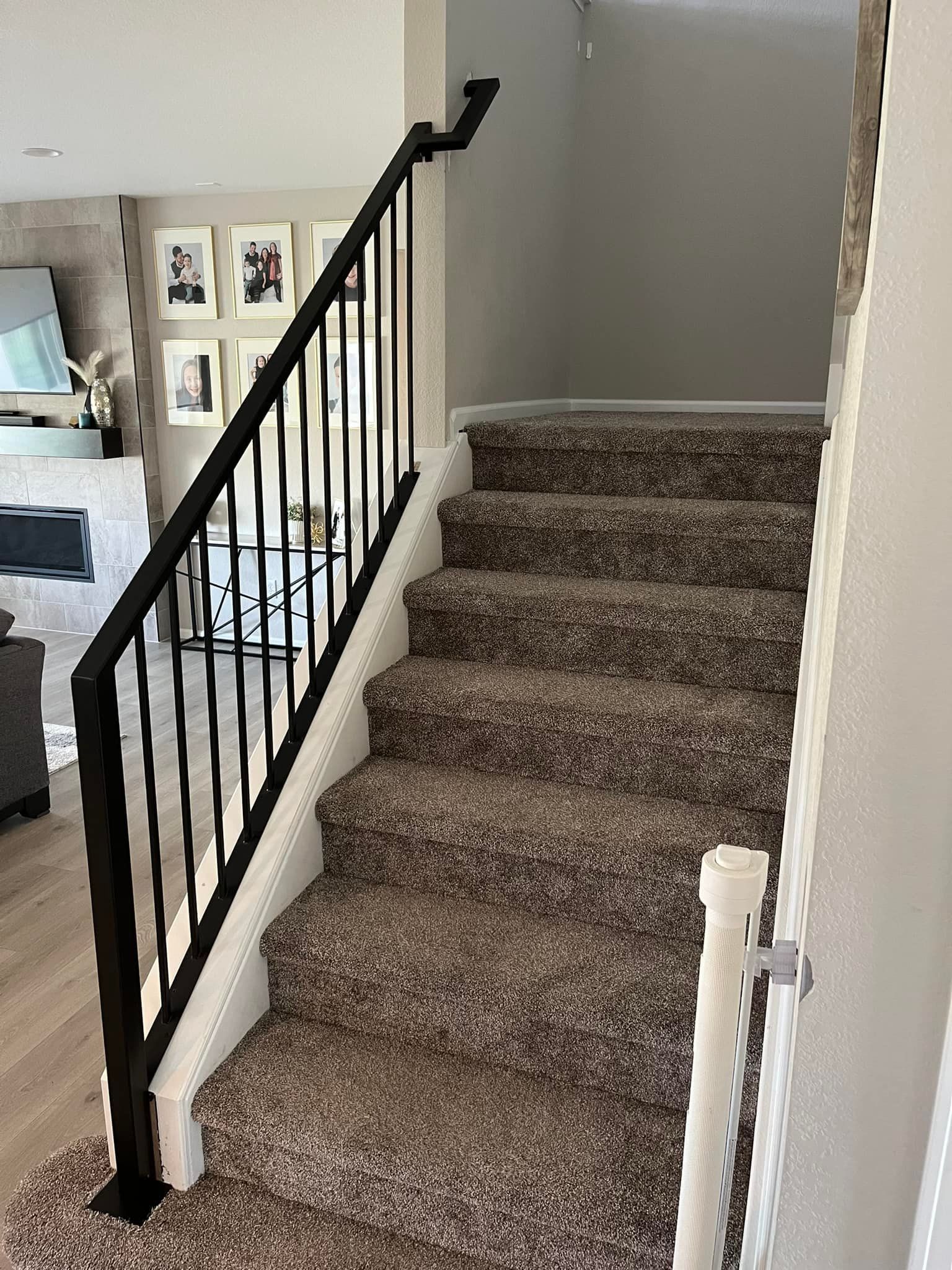 Staircase with brown carpet steps, black metal railing, and white trim.
