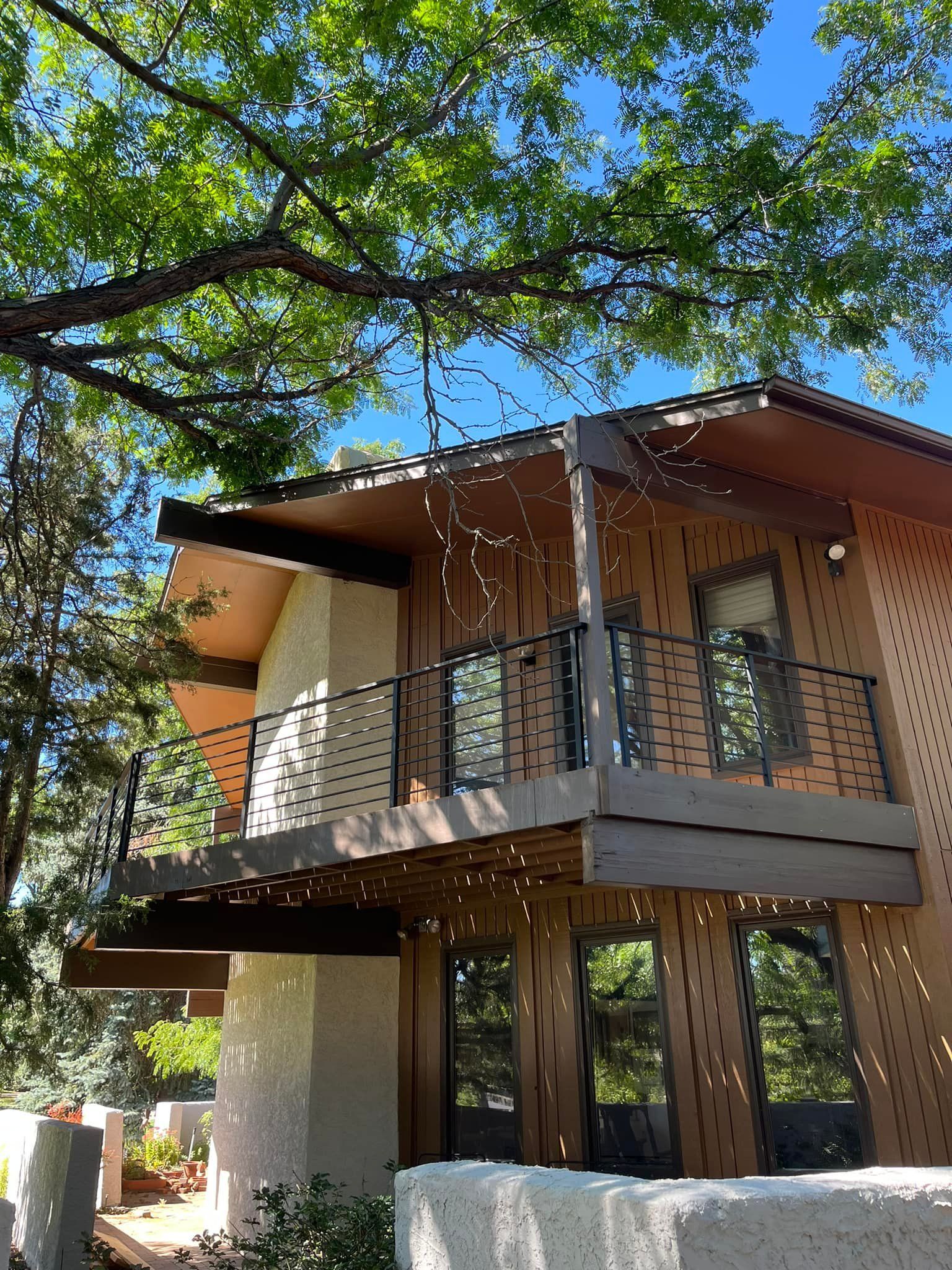 Two-story house with brown siding, balconies, and hanging lights under a tree with green leaves.