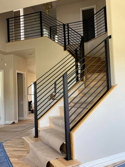 Black metal railing on a two-story staircase with light-colored wooden steps and tan walls.