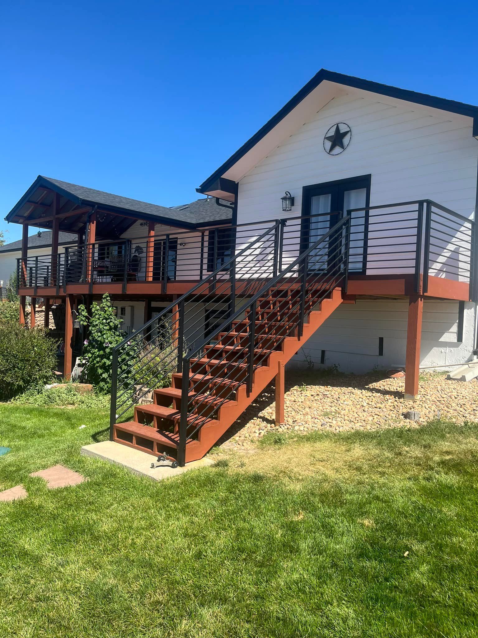 House with a wooden deck, stairs, and black metal railings. White siding and a green lawn.