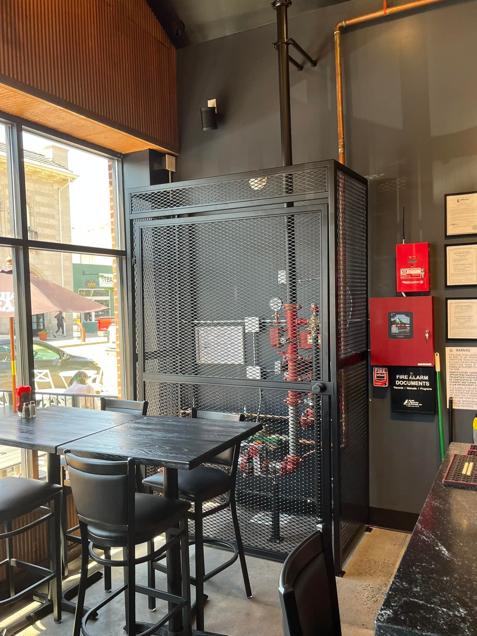 A black metal cage with a table and chairs in front of a window in a restaurant setting.