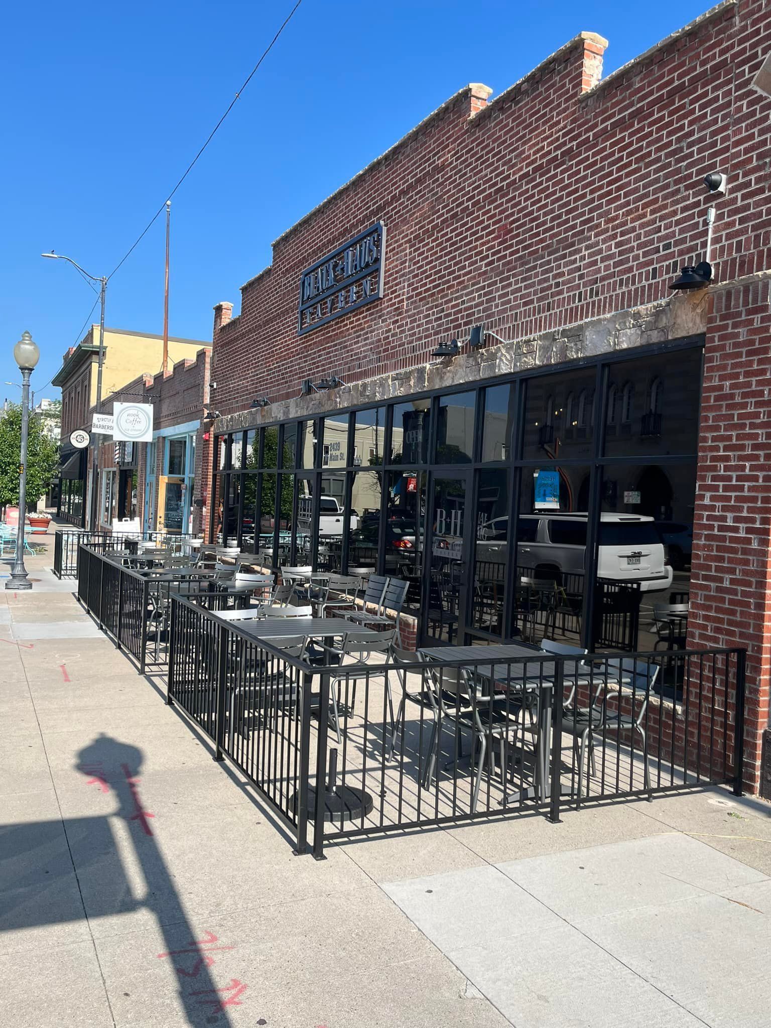 Restaurant exterior with outdoor seating, brick facade, glass windows, and black metal fencing.