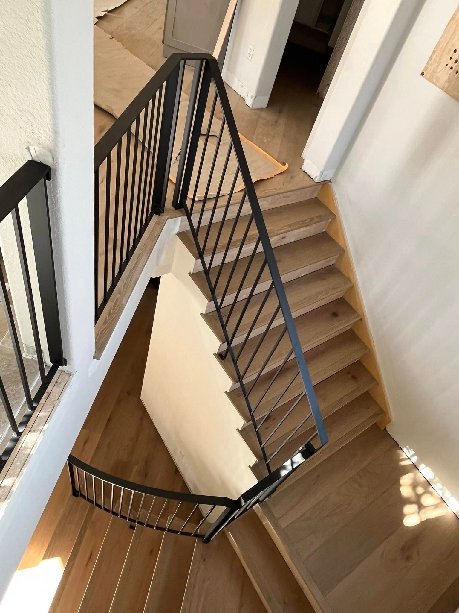 Overhead view of a modern staircase with wooden steps, black metal railings, and a bright hallway.