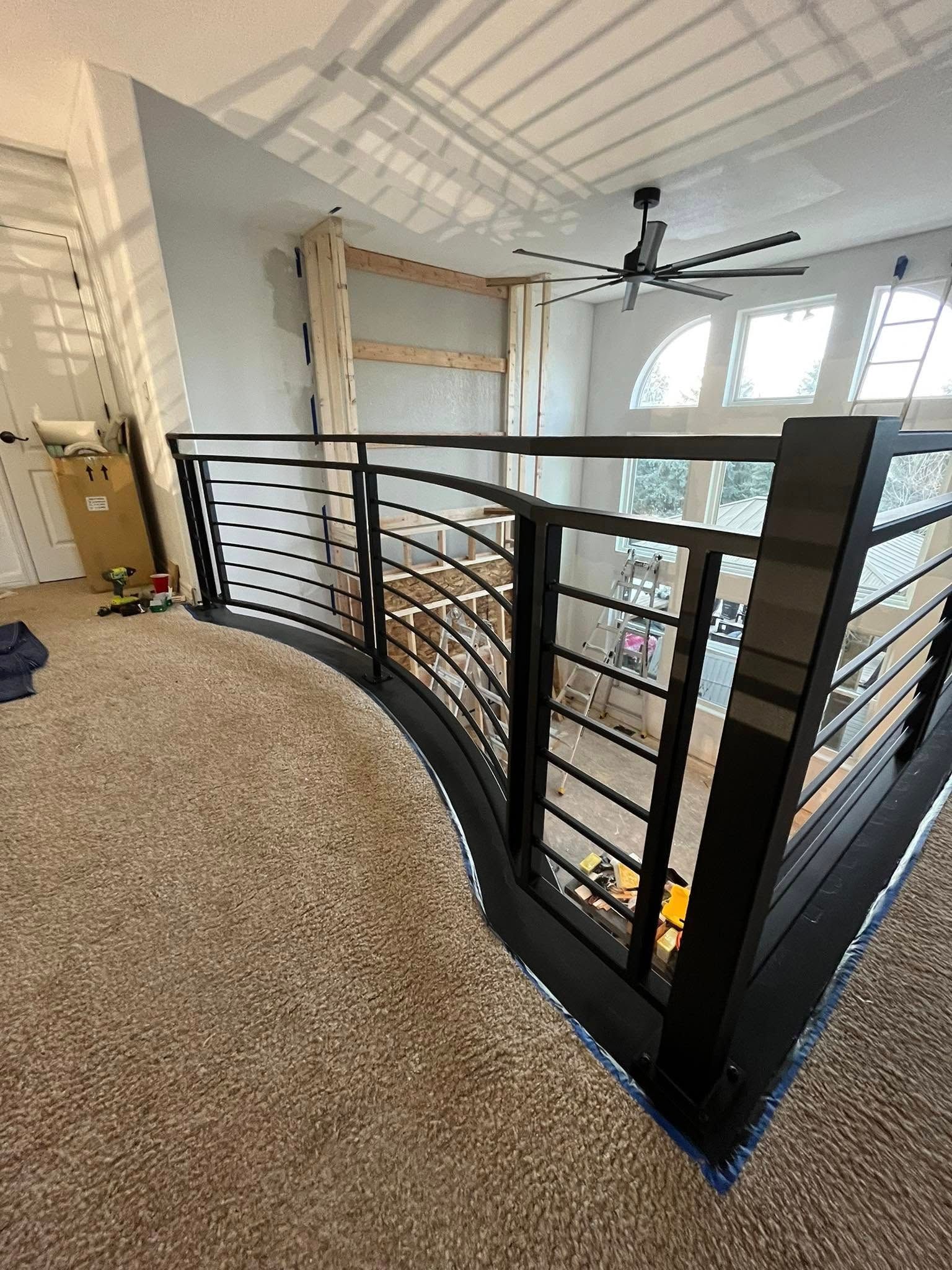 Interior view of a modern black railing with curved metal bars on a beige carpeted loft, overlooking a lower level.