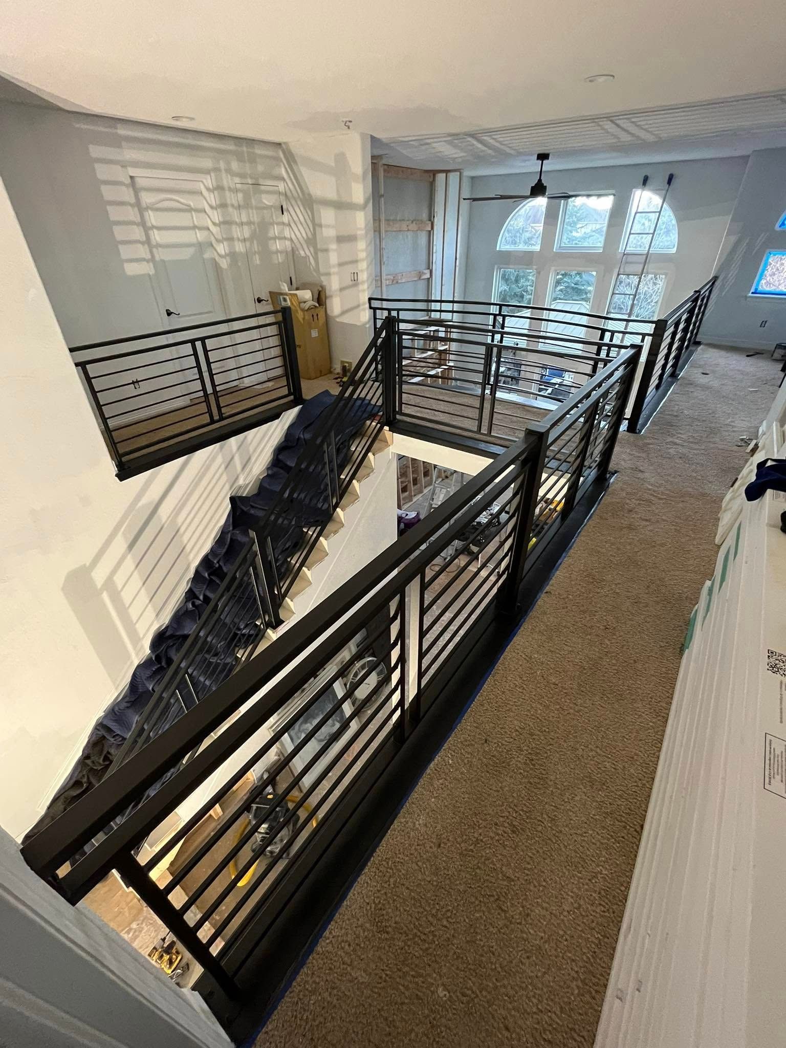 Interior view: staircase with black metal railings, leading up to a large window. Beige carpeted flooring.