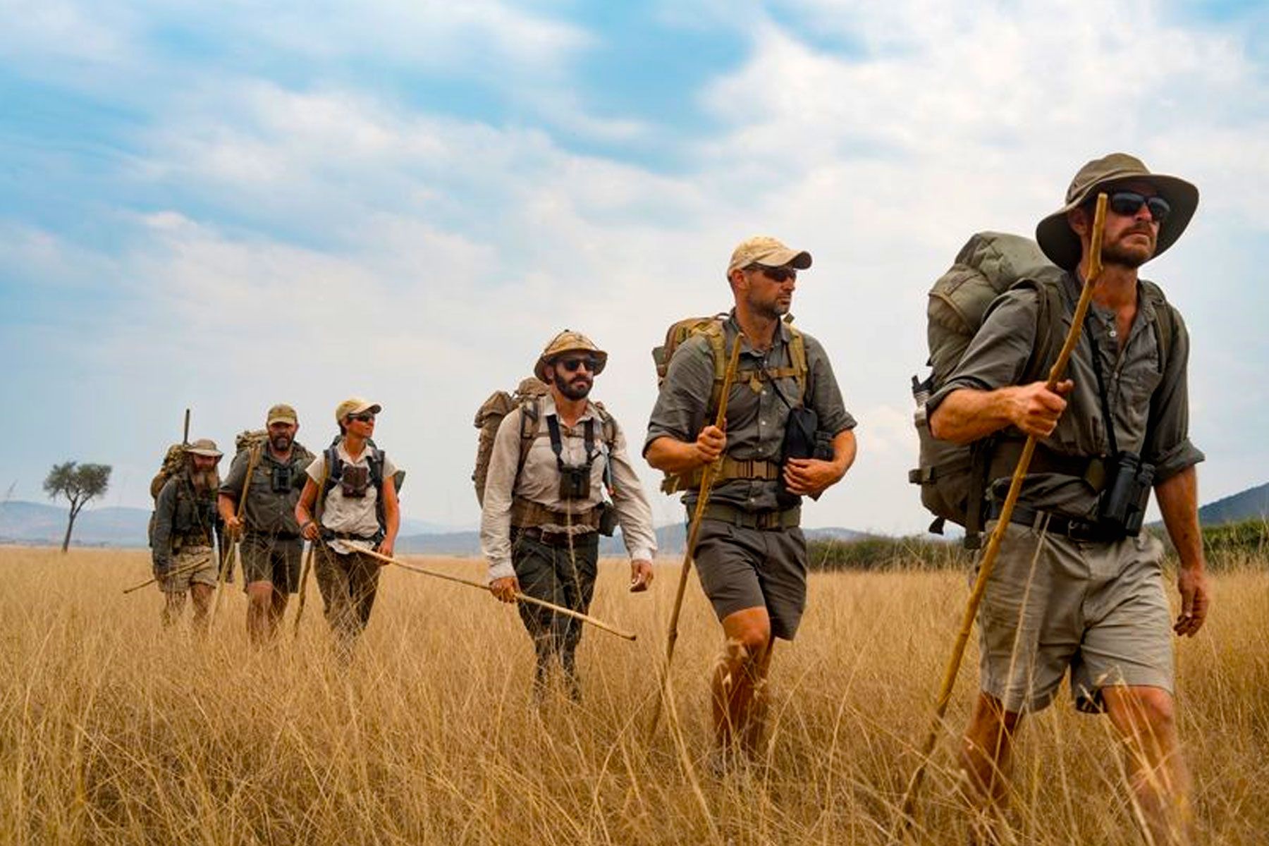 Tourists clad in full safari gear and sun huts hiking the savannah along Akagera's electric fence, part of a behind-the-scenes experience at the conservation of Akagera