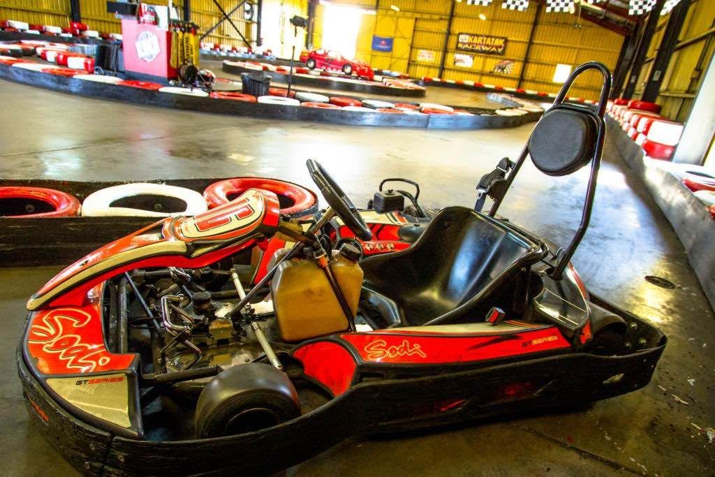 A red and black go kart is parked on the side of a race track.