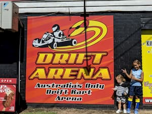 A couple of people standing in front of a drift arena sign.