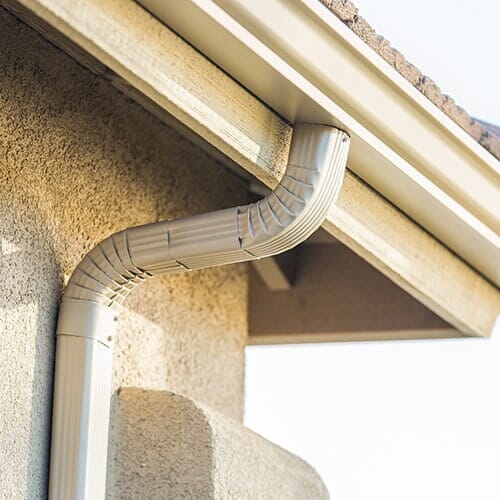 Beige gutter and downspout on a stucco house.