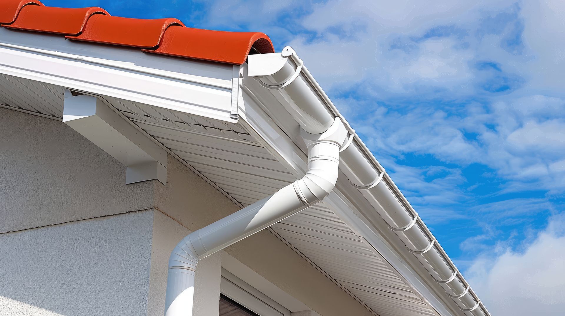 House roof with red tiles and white gutters against a blue sky.
