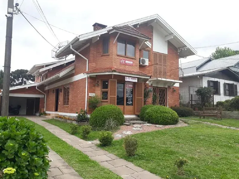 Prédio de tijolos de dois andares com detalhes em branco, gramado verde, entrada para carros e arbustos.