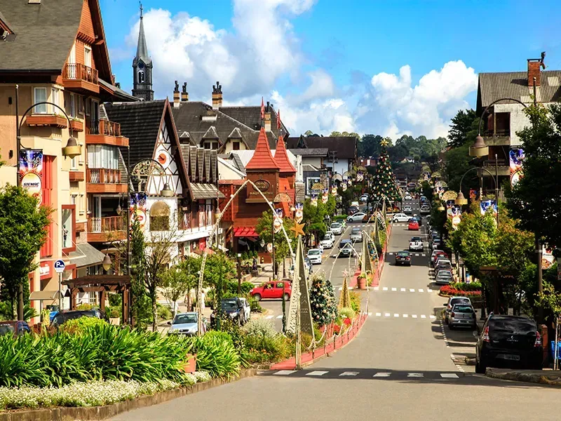 Cena de rua em uma cidade com arquitetura de estilo europeu, árvores, carros e céu azul.