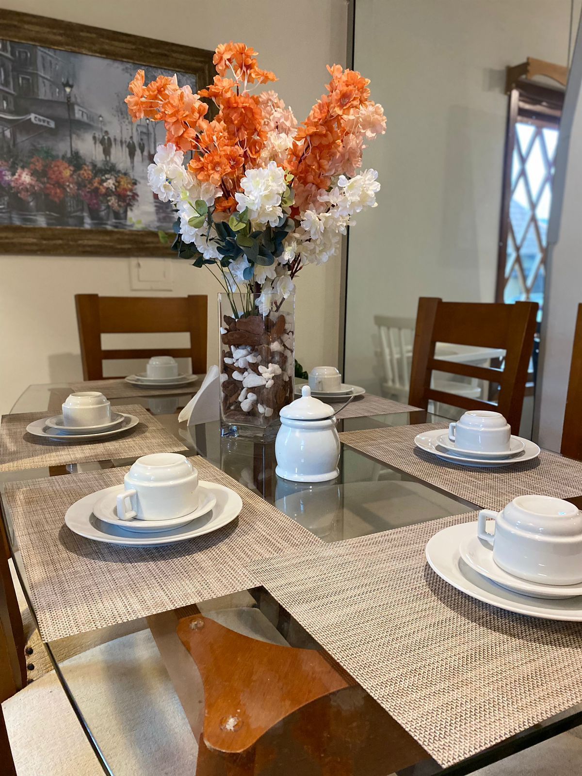 Conjunto de mesa de jantar com louça branca e arranjo floral como centro de mesa.
