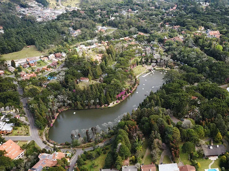 Vista aérea de um lago rodeado por árvores verdejantes, casas e uma estrada.
