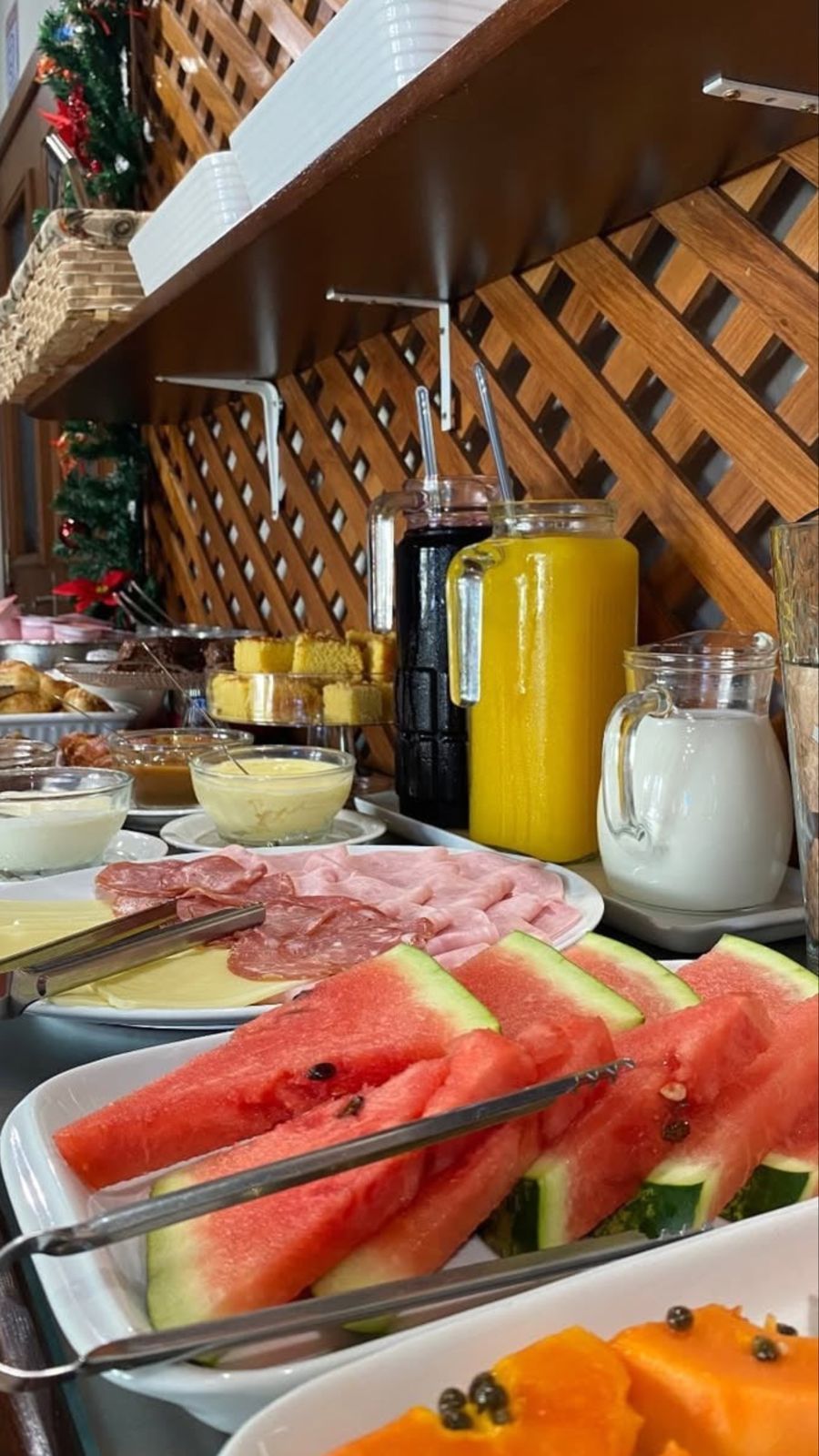 Buffet de café da manhã com melancia, suco de laranja e outros alimentos.