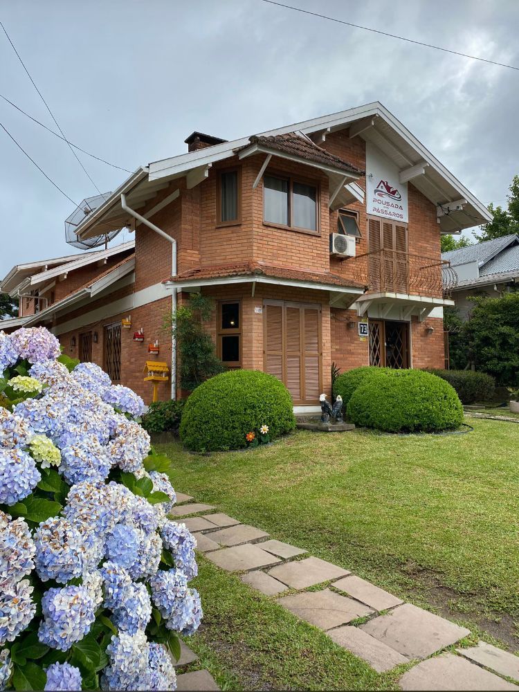 Casa de tijolos com telhado de telhas, gramado verde, hortênsias azuis e calçada de tijolos.