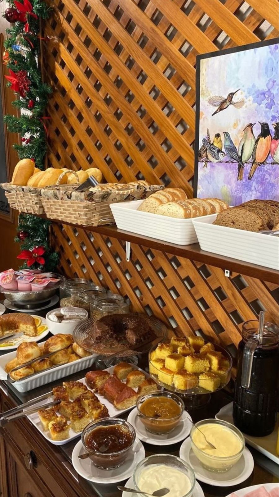 Buffet com diversos tipos de pães, bolos, geleias e manteiga expostos em uma bandeja de madeira.