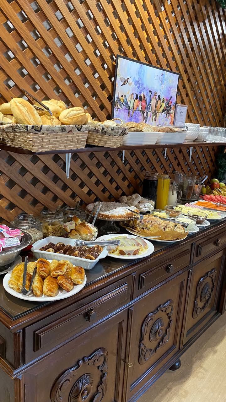 Mesa de buffet com diversos produtos de panificação e frutas expostos em prateleiras de madeira em um restaurante.