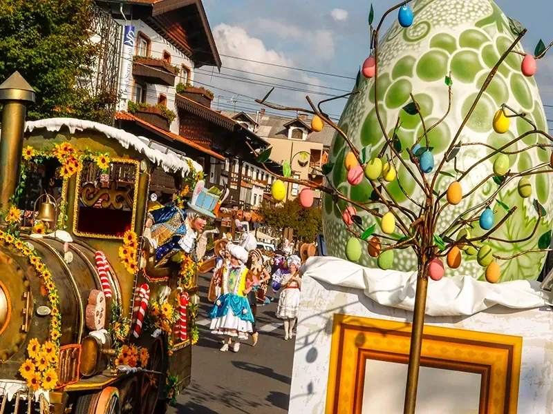 Desfile de Páscoa com trem decorado, árvore de ovos e pessoas fantasiadas em uma rua da cidade.
