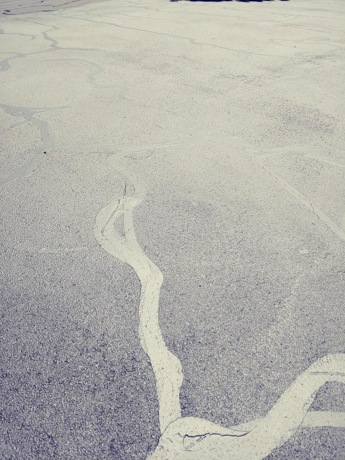 Cracked asphalt with light-colored streaks, possibly from water runoff.