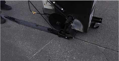 Black machine sealing a crack in asphalt pavement.