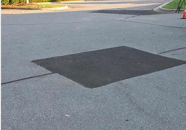 Square asphalt patch on a paved road surface.