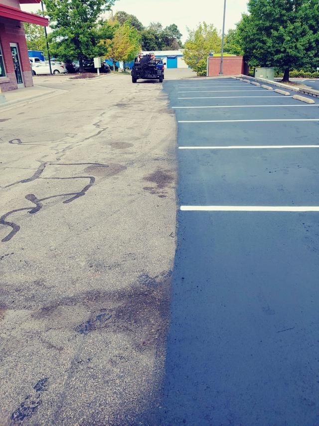 Half-paved parking lot. The left side is worn, the right side is freshly paved and marked with white lines. A car is visible.