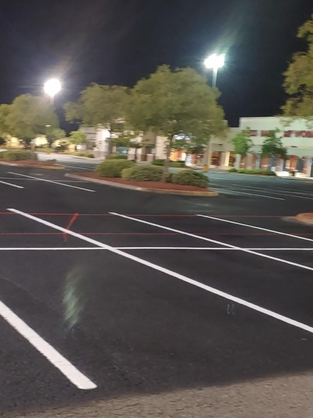 Empty asphalt parking lot at night with bright overhead lights and a building in the background.