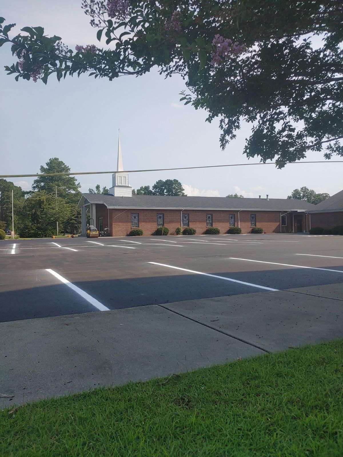 Parking lot in front of a brick building with a steeple visible in the background, under a blue sky.