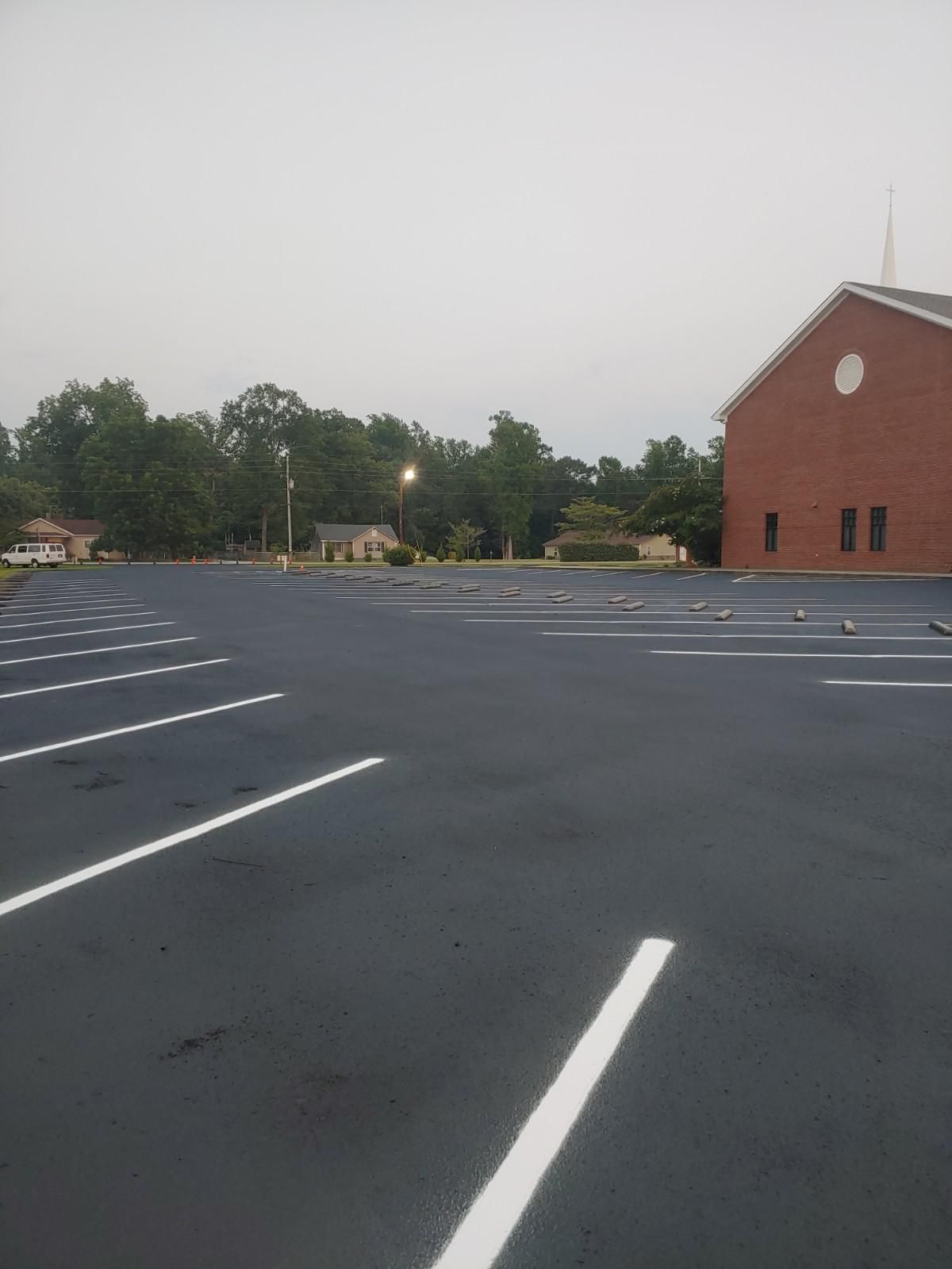 Empty parking lot with freshly painted white lines, brick building on right, trees in background.