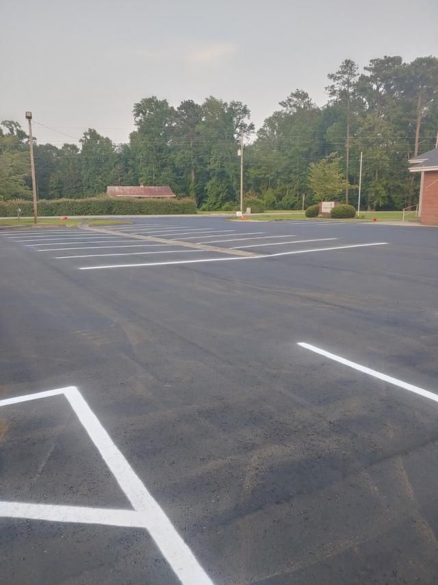 Empty parking lot with freshly painted white lines. Trees in the background, cloudy sky.